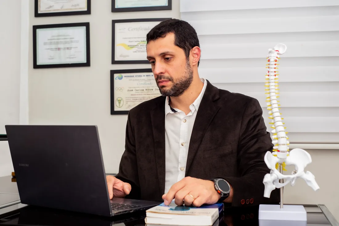 Dr. José Carlos analisando um caso ao lado de um modelo anatômico da coluna vertebral
